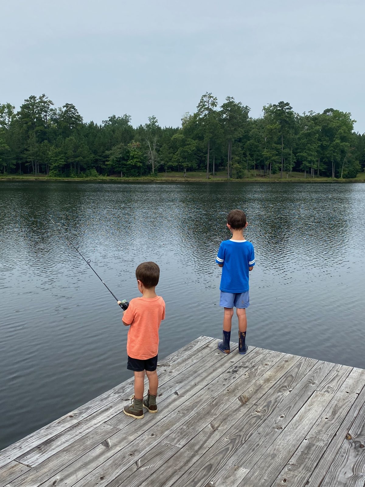 Two young anglers fishing from a dock on a clear, healthy pond